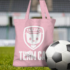 Pink tote bag with 'TAILSFC Team Cat' design on grass next to a soccer ball