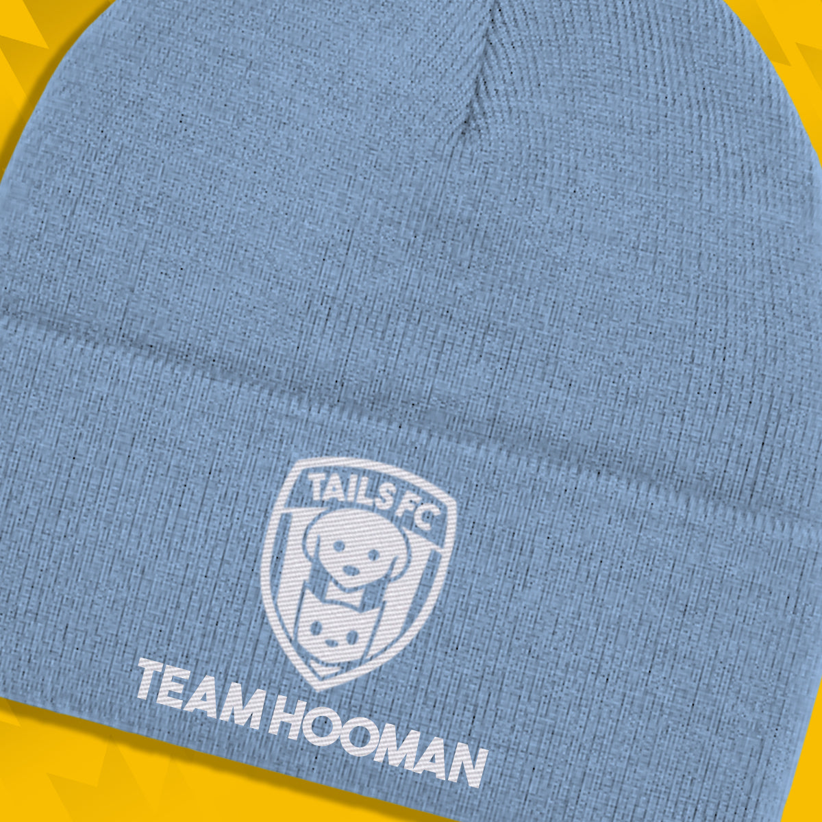 Blue beanie with 'TAILS FC' logo and 'TEAM HOOMAN' text on a yellow and blue gradient background