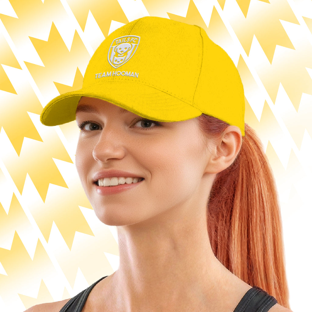 Woman wearing a yellow Tails FC cap with Team Hooman logo on a yellow background