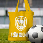 Yellow tote bag with 'TAILS FC' and 'Team Hooman' design on a grassy field with a soccer ball.
