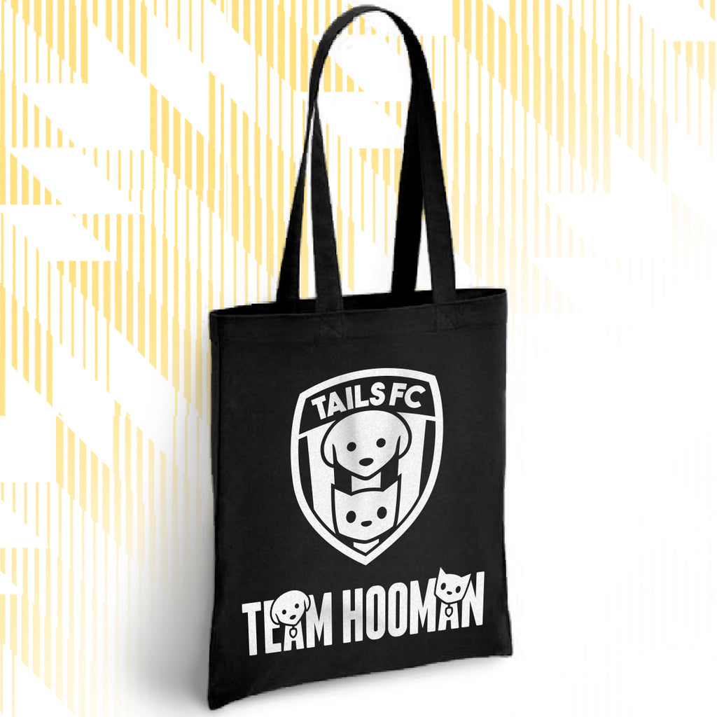 Black tote bag with 'TAILS FC' and 'Team Hooman' design on a white background with yellow abstract patterns.