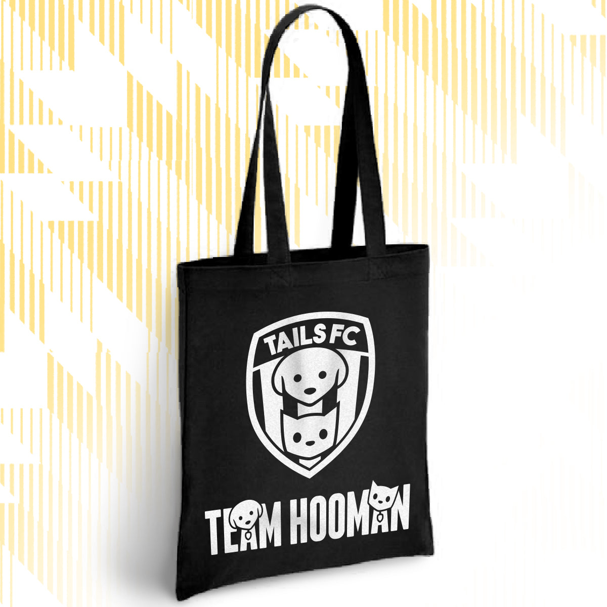 Black tote bag with 'TAILS FC' and 'Team Hooman' design on a white background with yellow abstract patterns.