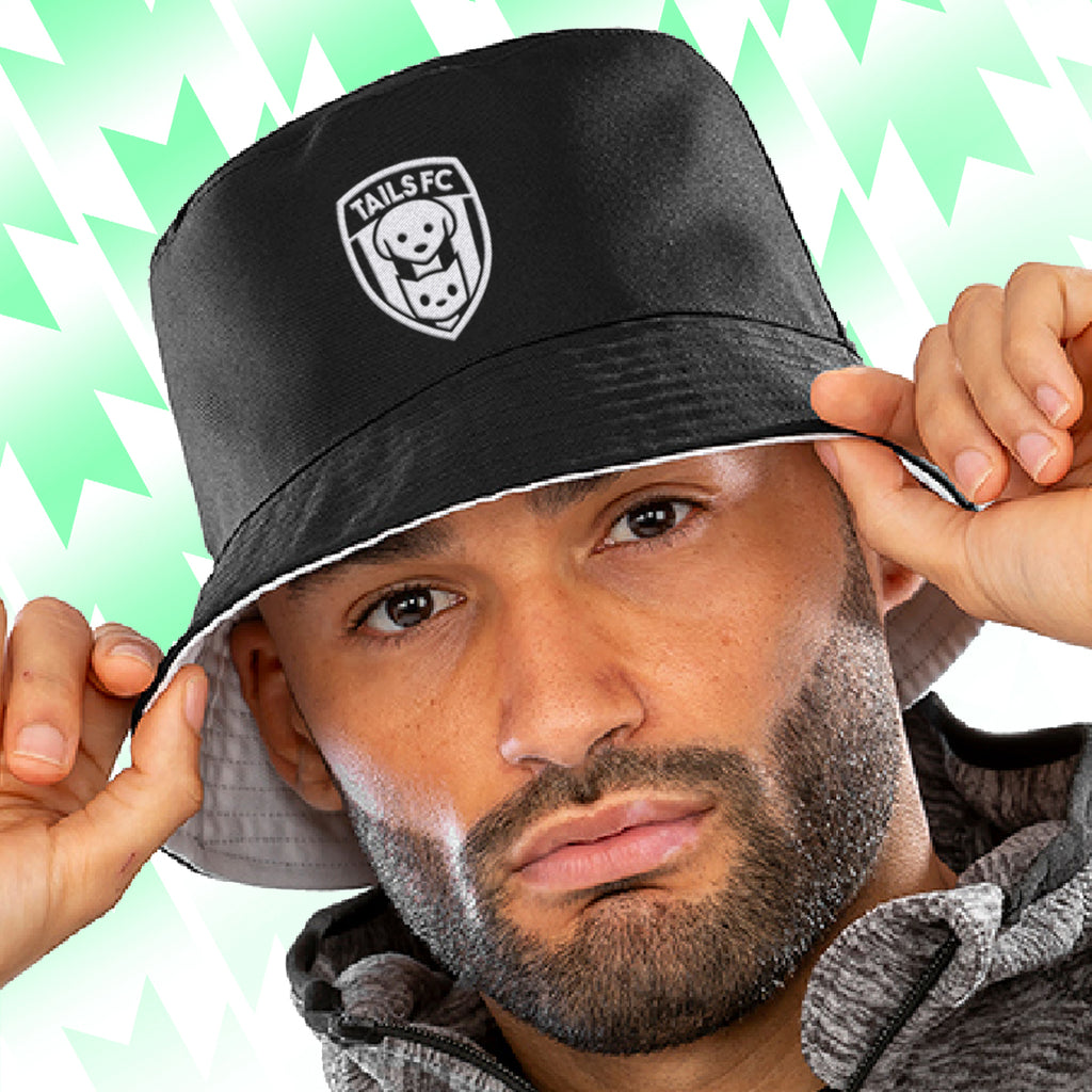Person wearing a black Tails FC bucket hat with a logo on a green and white patterned background