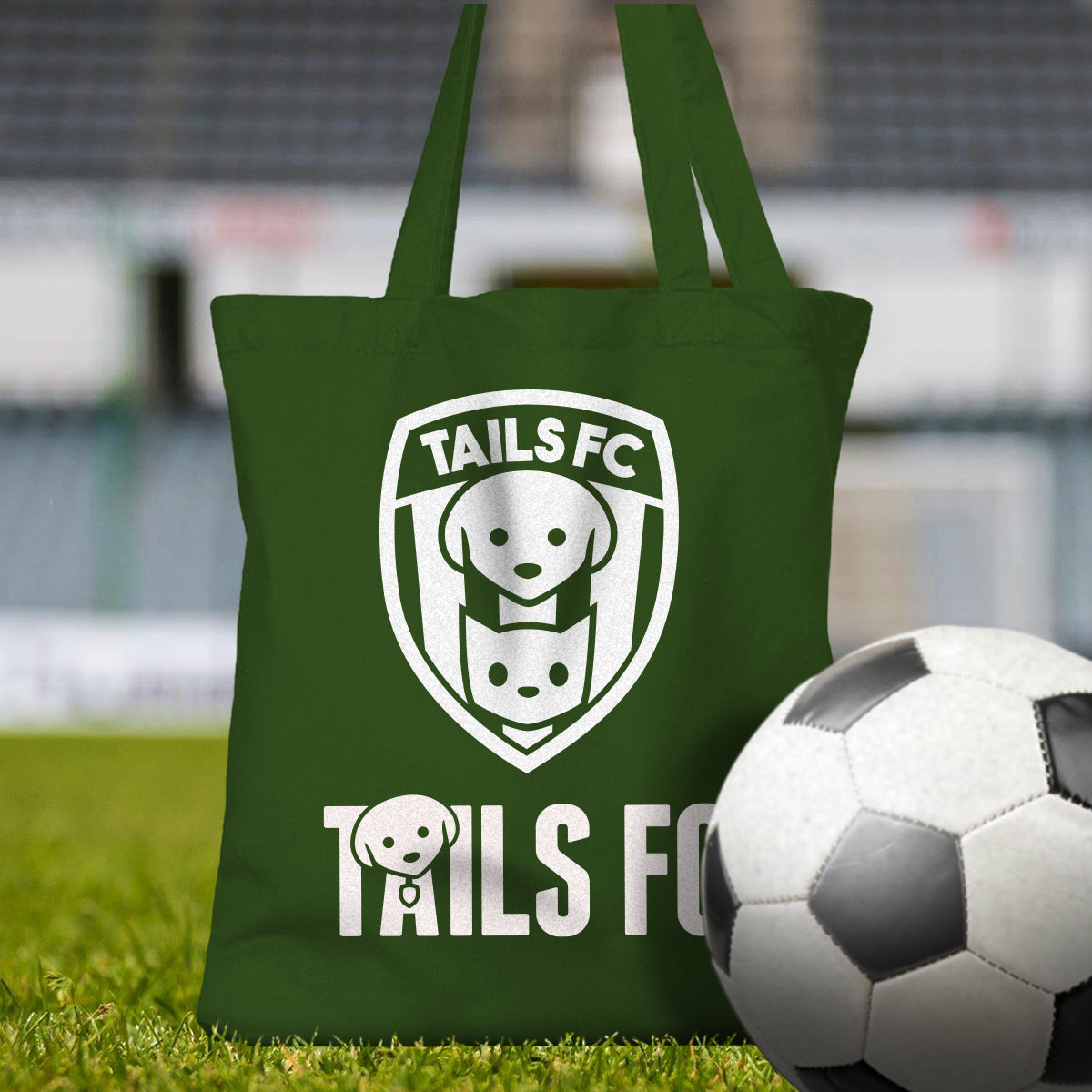 Green tote bag with 'TAILS FC' logo on grass with a soccer ball